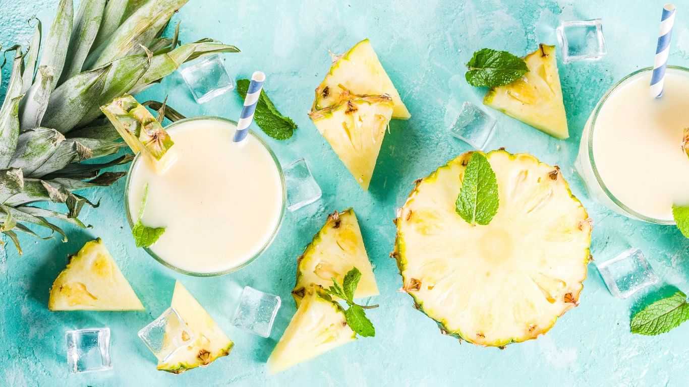 Pineapple slices, smoothies with mint, and ice cubes on light blue background.