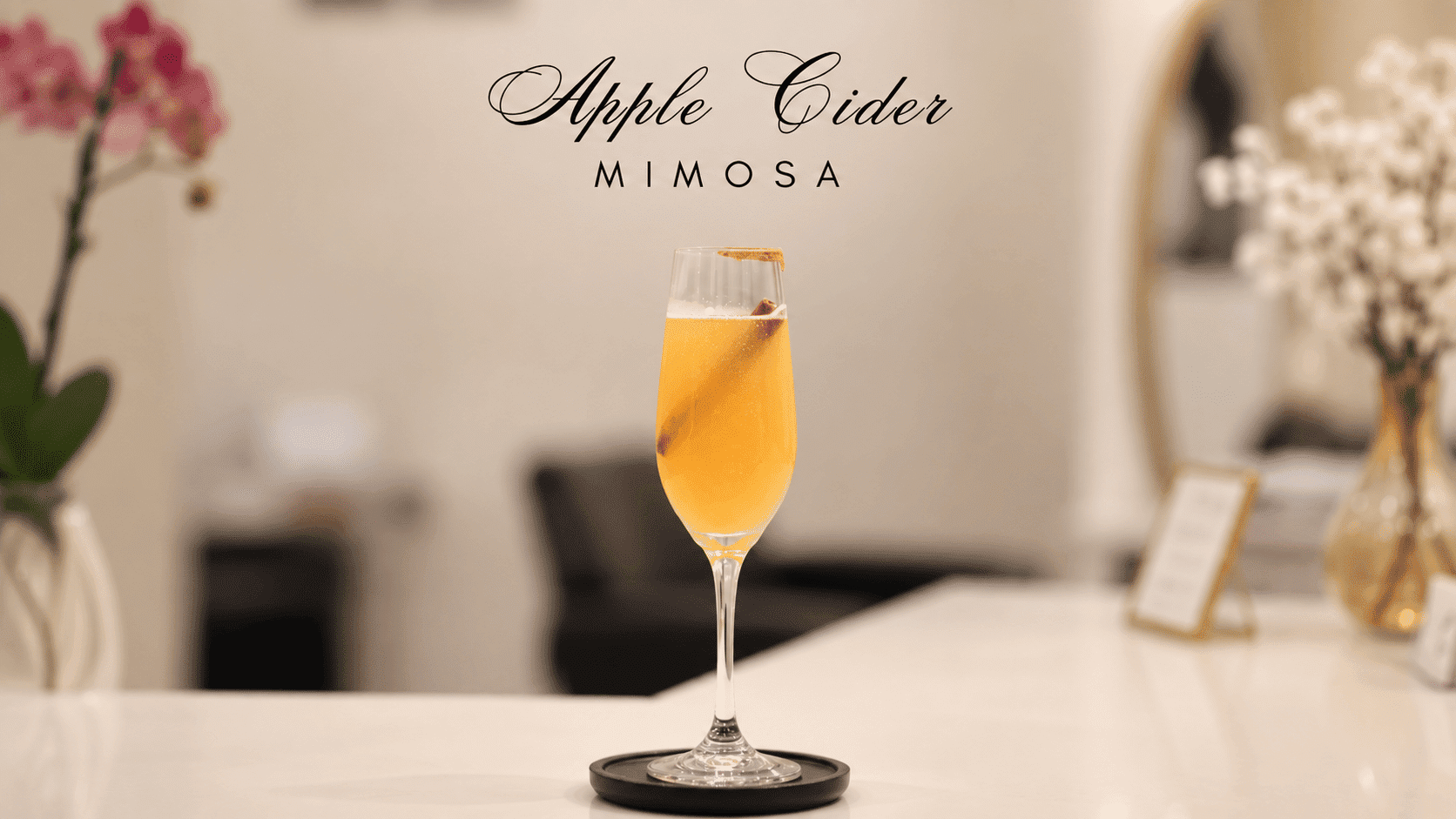 Apple cider mimosa in a tall glass with an orange garnish on a white countertop.
